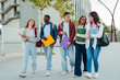 © Jose Calsina - A lively group of young students enjoying their time together, smiling and sharing laughter while carrying vibrant folders and notebooks as they walk on campus, showcasing friendship and camaraderie.