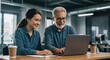 © Dian - Experienced senior businessman mentoring a young female colleague, working together on a laptop in a modern office.