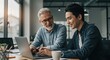 © Dian - Experienced senior businessman mentoring a young female colleague, working together on a laptop in a modern office.
