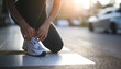 © waragron - A person ties their shoelaces while preparing for a run on a city street, with sunlight creating a warm, energetic atmosphere.