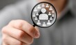 © rewa - Hand holds magnifying glass focusing on a person icon surrounded by other icons