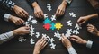 © DSGNCO - Diverse Hands Collaborating to Assemble Colorful Puzzle Pieces on Dark Wooden Table