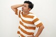 © DMH - confused young asian man looking up while scratching his head on white background