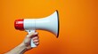 © MdShahid - Hand holding a white and red megaphone against a vibrant orange background