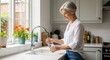 © W.O.W - Elegant woman pouring fresh water into a glass near kitchen sink. Healthy lifestyle and hydration concept. Modern kitchen interior.