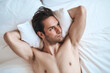 © Teodor Lazarev - A young man lies on a white bed, resting comfortably with his arms behind his head. He gazes upwards, reflecting peacefully in a bright and inviting room