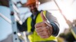© ryker - Construction worker in safety vest and hard hat gives thumbs up gesture while standing near ladder. image conveys sense of positivity and safety in work environment
