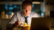 © Thuntaree - Late Night Meal and Work Focus of Man with Laptop in Home Office
