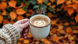 hand holding a hot mug of pumpkin spice latte with steam rising against a background of orange leaves and cozy knit sweater