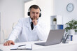 © New Africa - Doctor in headphones having online consultation via laptop indoors
