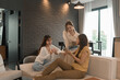 © MIND AND I - Three young Asian women shopping online at home using a laptop and credit card. They are smiling and enjoying time together in a relaxed and modern living room.