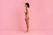 © Anastasiya - Side view shot of slim fit young black female in beige underwear standing on pink background. African American woman with toned body and beautiful curves posing in studio, copy space