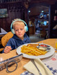 © Elena - Child with Headphones Eating Fries and Cutlet at Table