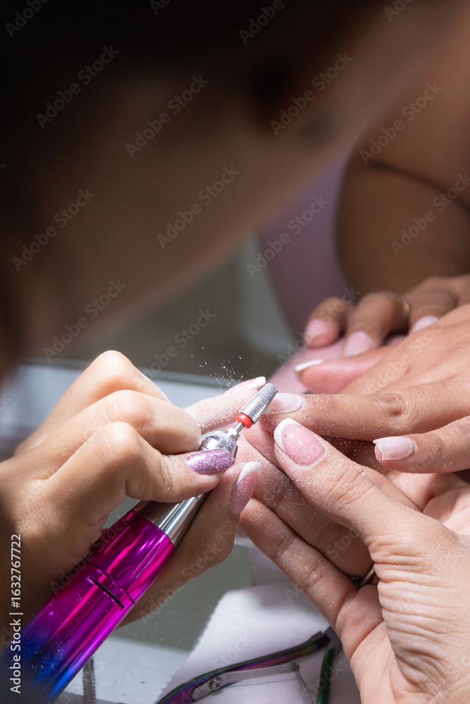 An unrecognizable woman is removing nail polish from a female client with an electric remover inside a beauty salon in Neiva, Huila, Colombia. A handmade and manicure concept