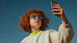 © utaem2022 - Young woman taking selfie with smartphone against blue sky