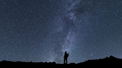 Wall Mural - Hiker silhouette stands on the hill on the  Milky Way galaxy  background. Night tight landscape starry sky.