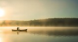 Silhouette of a person paddling a canoe on a tranquil, misty lake during a beautiful golden sunrise.