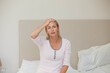 © wavebreak3 - Woman wearing pajamas sitting on bed at home holding forehead near lamp and glass