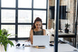 © Wavebreak Media - African American woman in olive green dress sitting at desk in office using laptop on stand