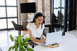 © Wavebreak Media - Chinese woman sitting at modern desk typing on silver laptop with potted plant and brown notebook