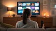 © Nimra - Woman sitting on a couch holding a remote control, watching a modern television screen with streaming apps in a cozy living room at night