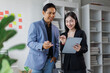© David - Two asian coworkers standing in the office discuss about business plan and looking at tablet.handsome asia man and beautiful asian woman as business partners working at indoor
