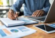 © Robert - A male professional of Asian descent is taking notes while analyzing data on his laptop, surrounded by graphs and charts, creating a focused and productive work atmosphere.