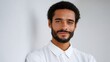 © BOJOShop - Portrait of a smiling man with a beard and curly hair wearing a white shirt leaning against a white wall
