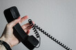 © Caroline - a person holding up a landline black telephone handset while lifting up the cord, considering technology options or providers. background with copy space