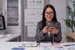 © crizzystudio - Asian businesswoman using smartphone and working with financial graphs at the office