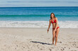 © WavebreakMediaMicro - Woman standing on sand near water edge wearing red bikini holding wooden boomerang, copy space