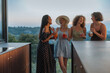 © bernardbodo - Four cheerful women laughing and drinking cocktails on a balcony at sunset