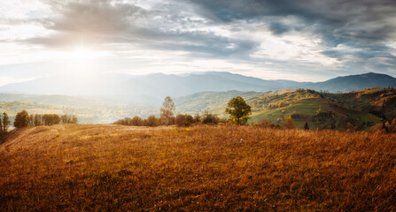Wall Mural - The sun breaks through the clouds and illuminates the autumn hills and valleys.
