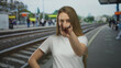 © Krakenimages.com - Young woman standing confidently at a train station platform with railway tracks in the background, smiling with hands on hips, enjoying an outdoor urban setting.