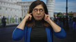 © Krakenimages.com - Woman covers ears with fingers in front of pisa tower building, wearing glasses and blue jacket; annoyance travel frustration.