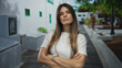 © Krakenimages.com - Young woman standing confidently on a city street with arms crossed, wearing casual attire, surrounded by modern urban architecture and green trees in an outdoor setting.