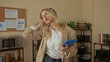 © Krakenimages.com - Young blonde woman celebrating with headphones and phone in a modern office interior, expressing joy and success in a workplace setting, highlighting a positive, energetic atmosphere.