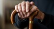 © ForAll - A close up of wrinkled hands gripping a wooden walking cane with a gold colored band around it