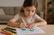 © The Little Hut - Focused Little Girl Coloring a Picture with Colorful Markers on a Table Indoors