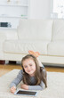 © wavebreak3 - School-age girl lying on stomach on fluffy rug in living room, using tablet with stylus