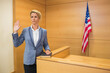 © WavebreakMediaMicro - Mid adult woman raising hand, resting on book at witness stand with American flag, copy space