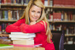 © WavebreakMediaMicro - Mid adult woman leaning on textbooks at library table with green notebook, eyeglasses, pink folder