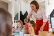 © lordn - Preschool teacher engaging with children at a table during an arts and crafts activity in a bright classroom