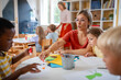 © lordn - Preschool teacher interacting with a diverse group of children during an arts and crafts activity, fostering creativity and multicultural learning.