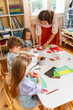 © lordn - Preschool teacher engaging with children at a table during an arts and crafts activity in a bright classroom