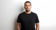 © Khasani - A confident young man with short dark hair and a beard, wearing a black t-shirt and looking at the camera against a white wall.
