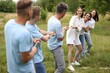 © New Africa - Team building. Group of happy people playing tug of war with rope outdoors