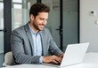 © MAJIDULISLAM - Professional businessman working on a laptop computer in a modern office smiling and engaged in his work achieving success and meeting deadlines