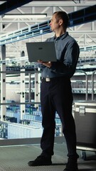 Poster - Vertical video Data center admin on industrial platform checks AI dashboard using laptop. Man in server farm tests artificial intelligence tools on notebook to ensure reliable performance, camera A