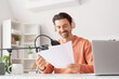 © Pixel-Shot - Male radio presenter with papers recording in studio